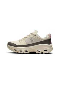 Lightweight sneaker with a beige upper, gray lower section, textured mesh, and contrasting red heel tab. Outsole features deep grooves for traction.