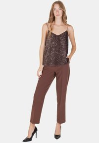 Top senza maniche con paillettes di colore marrone scuro, abbinato a pantaloni marroni. Il top presenta dettagli intricati con paillettes; i pantaloni hanno una vestibilità sartoriale.