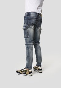 Džíny typu cargo z vybledlého modrého denimu s více bočními kapsami a úzkým střihem. Kombinované s černými, béžovými a zelenými sportovními teniskami.