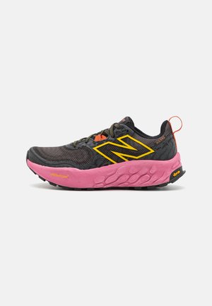 Schwarzer Trailrunning-Schuh mit pinker Außensohle, gelben Akzenten und grauem Mesh-Obermaterial. Verfügt über eine verstärkte Zehenkappe und strukturiertes Schnürsystem.