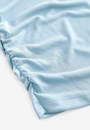 Tissu bleu clair avec une texture douce, présentant des détails froncés sur le bord. Matériau lisse et extensible, adapté à une tenue décontractée.