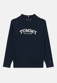 Granatowy sweter w warkoczowy splot z białym napisem "TOMMY HILFIGER" z przodu oraz małym logo Tommy Hilfiger na mankiecie rękawa.