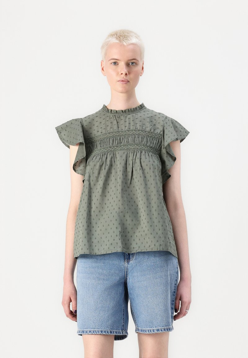 Grøn bomuldsbluse med flæseærmer, samlet bodice, prikmønster og høj halsudskæring. Sættes sammen med denimshorts.