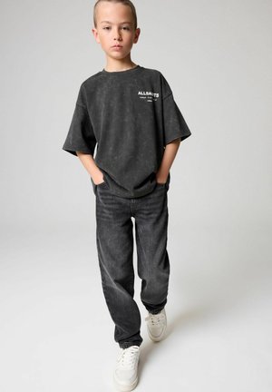 Grå oversized T-shirt med vit logotyp, tillsammans med mörkgrå jeans och vita sneakers. Slät textur, avslappnad passform.