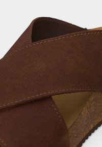 Καφέ σουέντ πλατφόρμα σανδάλι με φαρδιές διασταυρούμενες λωρίδες και σόλα με υφή φελλού σε λευκό φόντο.