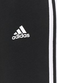 Svart tyg med vitt Adidas-logotyp och två vertikala vita ränder på höger sida, typiskt för sportkläder.