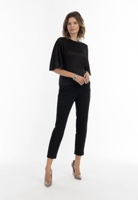 Top negru cu mâneci scurte, cu o textură netedă, asociat cu pantaloni negri slăbici. Modelul poartă tocuri bej ascuțite și o brățară cu accente argintii.
