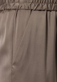 Zbliżenie na taupe tkaninę z marszczonym elastycznym pasem i boczną kieszenią na gładkim, lekkim materiale.