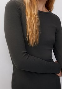 Maglia a maniche lunghe in cotone ribbed grigia scura con scollo rotondo, caratterizzata da una silhouette aderente e una texture di tessuto liscia, vista parzialmente su una figura.