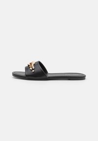 Svart platt flip-flop sandal gjord av slitstarkt läder, med ett brett rem som pryds av en guldfärgad dekorativ detalj framtill.