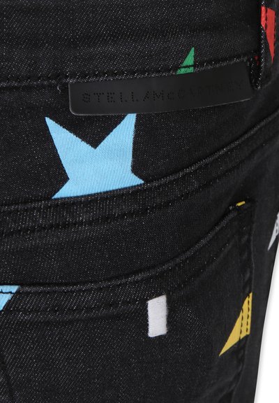 Jeans in denim nero con motivi a stelle colorate in blu, rosso e giallo, dotati di un'etichetta in pelle nera con marchio sulla tasca posteriore.