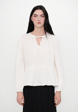 Blouse blanche à manches longues avec un col rond, un détail à nouer et une taille peplum. Fabriquée en tissu doux et lisse avec des accents froncés à l'ourlet.