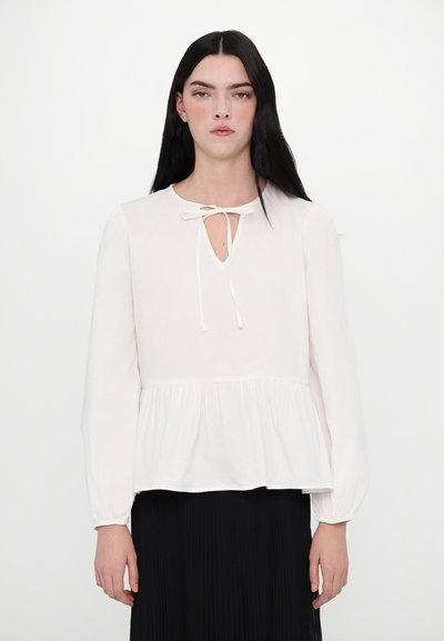 White long-sleeve blouse with a round neckline, tie detail, and a peplum waist. Features soft, smooth fabric and gathered accents at the hem.