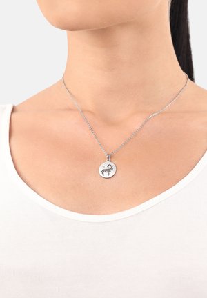 Primo piano del collo di una donna che indossa una collana in argento con un pendente rotondo inciso con un disegno di ariete.