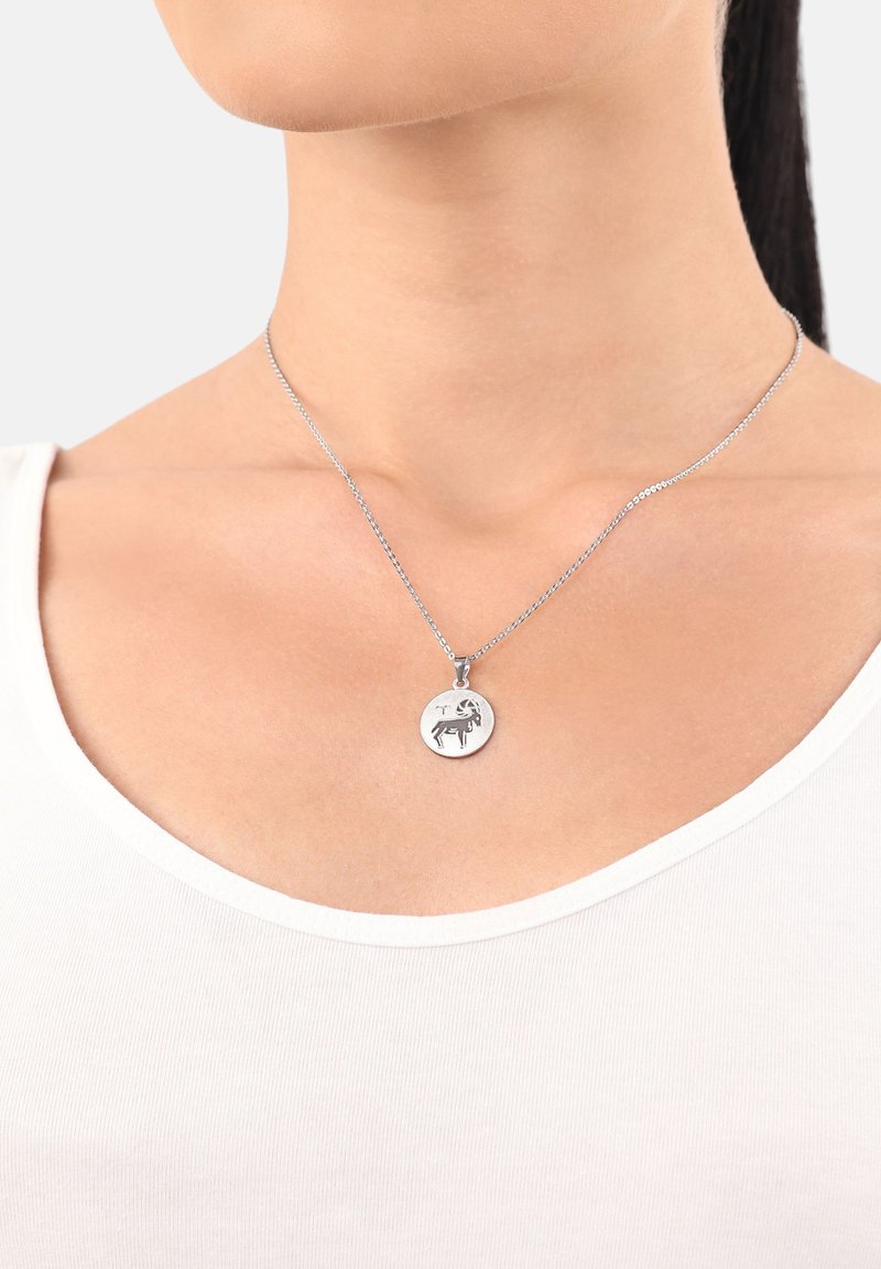 Primo piano del collo di una donna che indossa una collana in argento con un pendente rotondo inciso con un disegno di ariete.