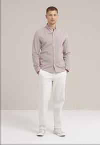 Camisa de cuadro rojo y blanco, tipo botón, con mangas largas, combinada con pantalones blancos y zapatillas ligeras. Diseño sencillo, sin patrones.