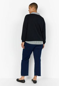 Maglietta nera a maniche lunghe con colletto a righe, abbinata a jeans blu tagliati con orli sfilacciati e ballerine in rete nera.