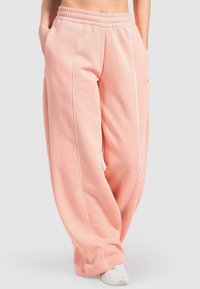 Rosa Jogginghose mit lockerem Schnitt, ausgestattet mit weißen Akzenten und Seitennähten. Der Stoff ist weich und ideal für Freizeitkleidung.