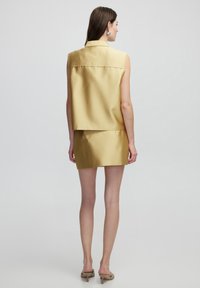 Sleeveless light yellow cropped vest with matching mini skirt. Smooth satin texture, minimal stitching, and a classic collar design.