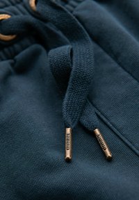 Pantalones joggers azul marino con textura tejida, que cuentan con ojales metálicos y cordones rematados en bronce grabados con "Dintibre."