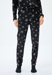 Mustat fleece-pyjamat, joissa on hopeinen tähti-kuvio, joustava vy�ötärö, jossa on naru, ja kootut nilkat. Pehmeä rakenne.