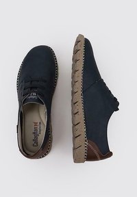 Zapatos de ante azul marino con acentos de cuero marrón, que presentan una suela de goma texturizada con un patrón moteado y costuras en contraste.