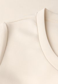 Helles beige Baumwollhemd mit Rundhalsausschnitt, glatter Textur und kurzen Ärmeln ohne sichtbare Muster oder Beschläge.
