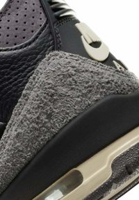 Sneaker in suede grigio e pelle nera con accenti testurizzati, unità d'aria prominente nella suola intermedia e elementi di design unici.