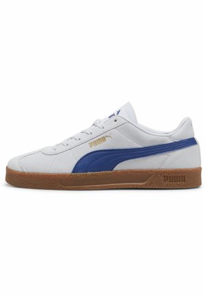Zapatilla de ante blanca con acentos azules, suela de goma y diseño de cordones. Presenta el logo dorado de "Puma" en el costado y en el talón.