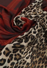 Rød og beige tørklæde med et ternet design, der har orange linjer og leopardmønster. Blød tekstur med flydende, lagdelt stof.