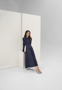 Completo in denim blu navy con top strutturato e pantaloni a gamba larga. Texture liscia, leggero splendore. Indossato con tacchi a punta grigio chiaro.