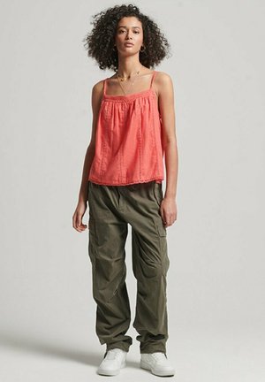Light coral sleeveless top with gathered neckline; paired with loose olive green cargo pants; worn with white sneakers.