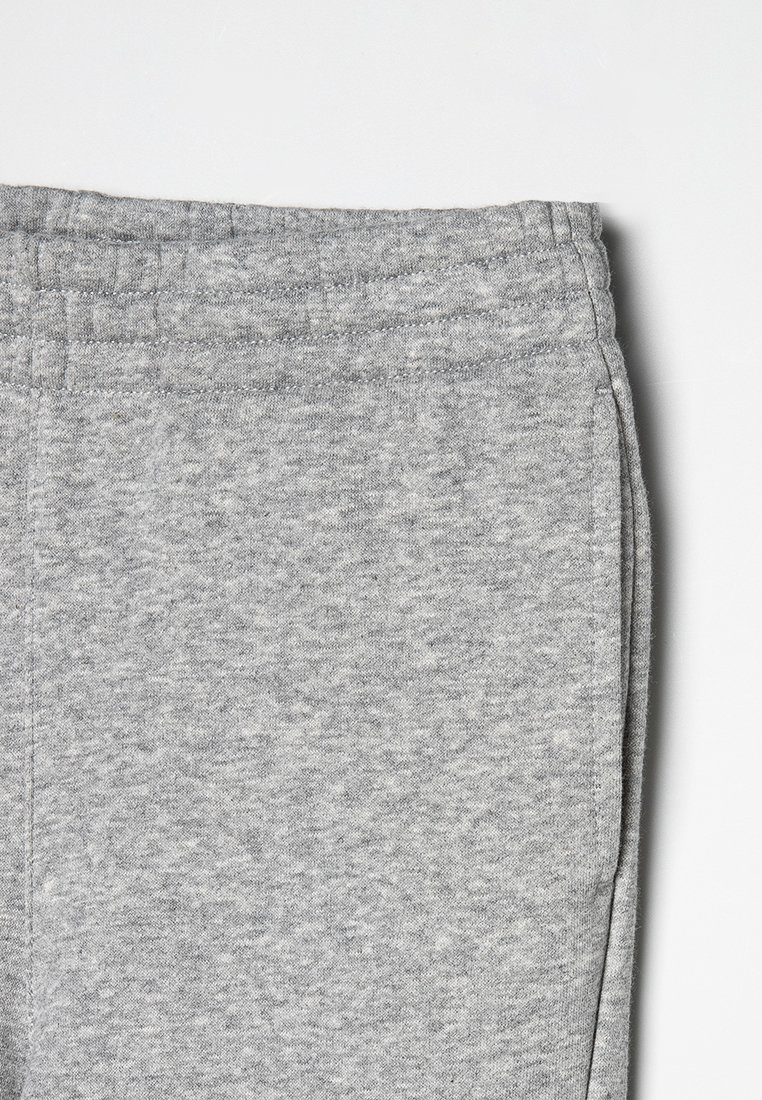 Close-up van de tailleband en bovenste gedeelte van grijze sweatpants met zichtbare stiksels en zachte stoftextuur op een effen achtergrond.