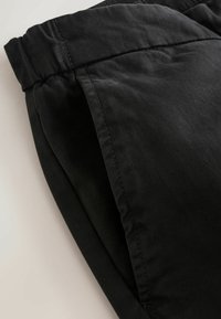 Black pants with a smooth, matte texture and elastic waistband. Features a side pocket and a tapered leg design.