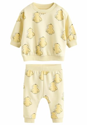 Completo in cotone giallo composto da due pezzi, con una maglia a maniche lunghe e pantaloni, entrambi decorati con una stampa di pulcini. Polsini e vita a coste.