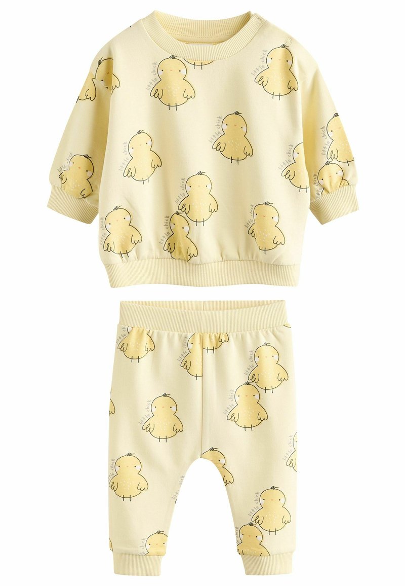 Dzeltena kokvilnas divdaļu komplekts, kas ietver garām piedurknēm topu un bikses, abiem ar vistas druku. Ribotas aproces un jostasvieta.