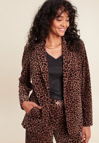 Blazer en velours marron à motif léopard avec une coupe décontractée. Comprend des revers crantés, des poches latérales et une texture douce. Assortie à un top noir.