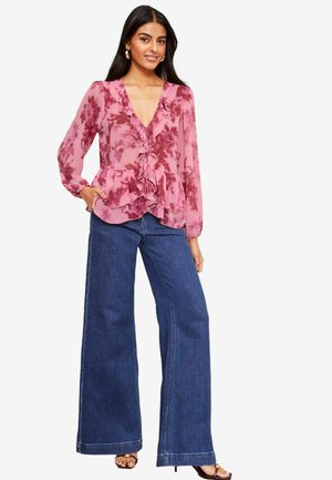 Pink floral print blouse with ruffled neckline, paired with wide-leg blue denim jeans. The look is completed with strappy sandals.