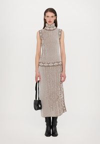 Haut sans manches en maille brun clair avec un motif texturé ; associé à une jupe longue assortie et des bottes noires hautes. Sac à main noir inclus.