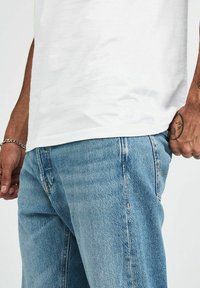 Vit bomullströja matchad med ljusblå denimjeans. Jeansen har en klassisk femficksdesign och synliga sömnadsdetaljer.