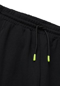 Czarne dresowe spodnie z elastycznym pasem, z czarnymi sznurkami zakończonymi neonowymi zielonymi końcówkami na białym tle.