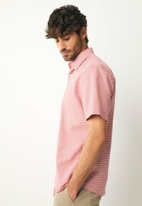 Chemise à manches courtes rouge avec un motif d'étoiles blanches. Confectionnée en tissu léger, elle présente un col boutonné et une coupe standard.