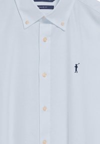 Jasnoniebieska bawełniana koszula o regularnym kroju. Posiada kołnierzyk z guzikami, beżowe guziki i granatowe haftowane logo przedstawiające postać trzymającą kij golfowy.