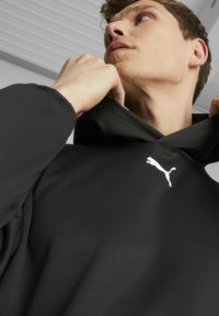 Sudadera con capucha negra de textura suave, con un logo blanco de Puma en el pecho; diseñada con cuello alto y un ajuste relajado.