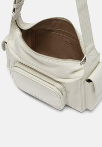 Borsa in pelle beige con scomparto principale con zip, tasca frontale e cuciture decorative. L'interno è foderato di marrone.