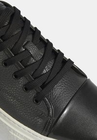 Schwarze Sneaker mit einem strukturierten Lederoberteil und glatten Akzenten, robusten schwarzen Schnürsenkeln und einer weißen Gummisohle.