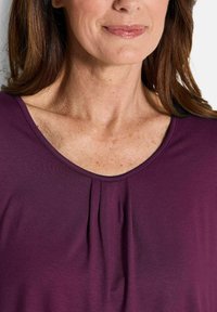 Lila Bluse mit Rundhalsausschnitt, ausgestattet mit einer Faltenoptik auf der Vorderseite und einem glatten, weichen Stoffgefühl.