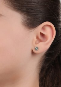 Örhängen med en blommig design och en central grön sten omgiven av mindre klara stenar, satta i metall med en polerad yta.