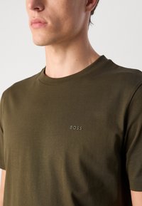 T-shirt en coton vert olive avec col rond, manches courtes et logo "BOSS" discret sur le haut à gauche. Texture douce, design ajusté.