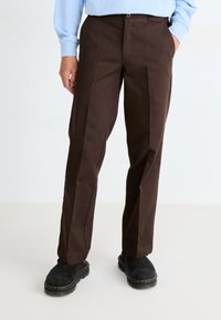 Pantalones marrones con un corte recto, textura suave y bolsillos delanteros. Combinados con botas negras con costuras amarillas.